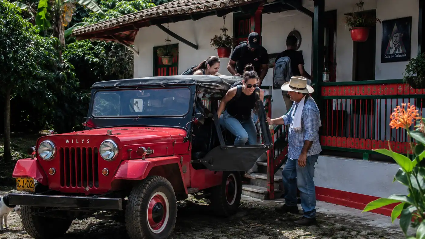 Pasajeros bajándose de un Willys frente a una finca cafetera